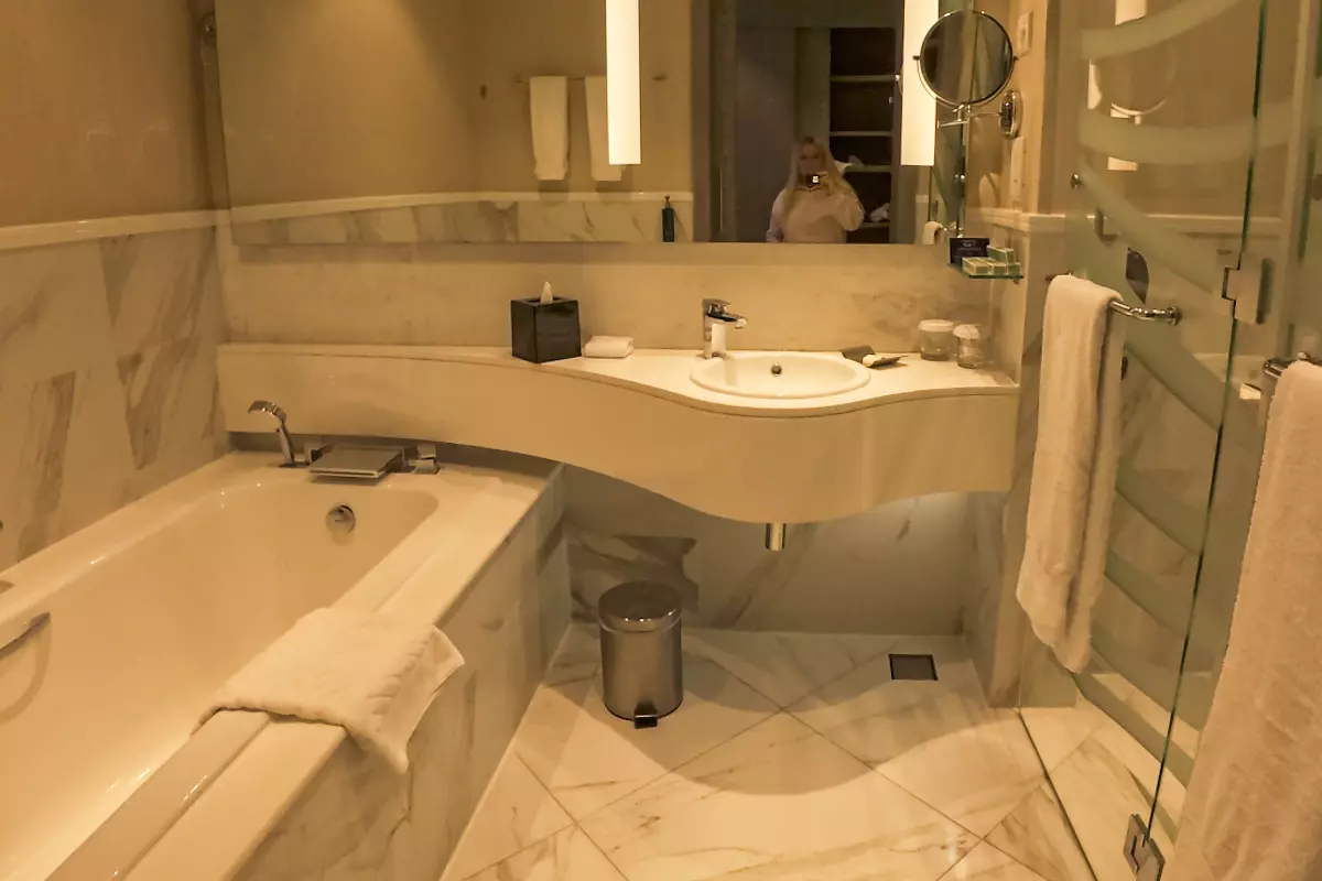 Modern bathroom at DoubleTree by Hilton Doha – Old Town featuring a bathtub, marble surfaces, curved vanity with sink, and neatly arranged towels