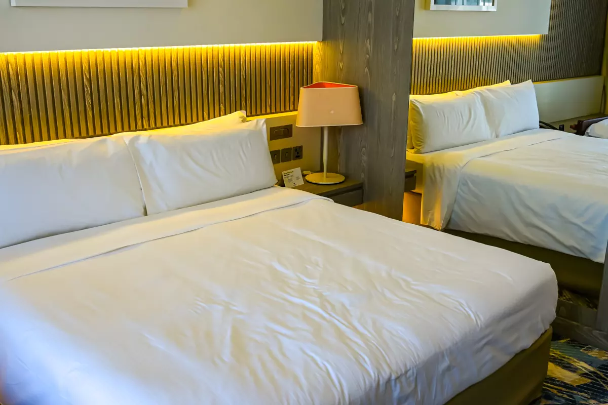Guest room at DoubleTree by Hilton Doha – Old Town featuring two neatly made beds, warm accent lighting, bedside lamp, and modern wooden decor