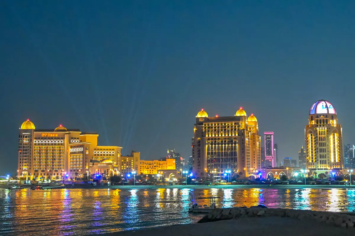 Night view of the illuminated St. Regis hotel by the water in Katara.