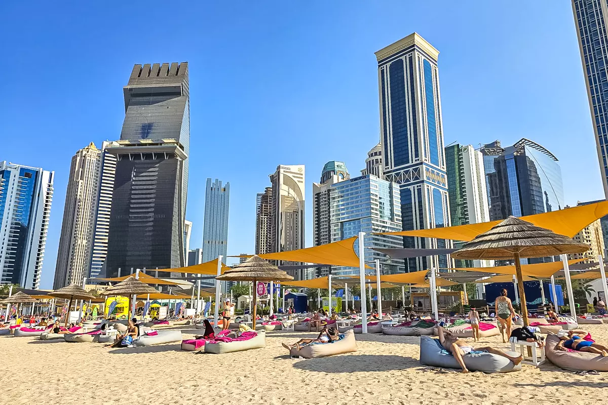 Beachgoers relaxing on a sandy beach with Doha’s West Bay hotels and skyscrapers in the background.